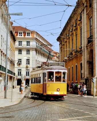 A yellow train in on a rail road surrounded by building in Lisbon, Portugal