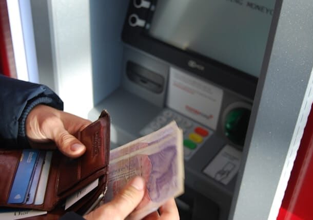 Man withdrawing cash at an ATM and putting the cash in his wallet - offshore banking wealth building benefits
