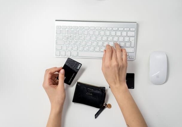 Person making an online payment using a credit card while typing on a white keyboard