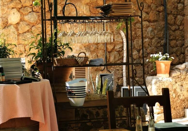 A Spanish restaurant with a brick wall, wooden chairs, and glasses hanging on a metal shelf.