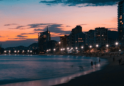Orange sunset in Puerto Vallarta, Mexico with people walking on the beach and buildings in silhouette - North American beaches to retire near