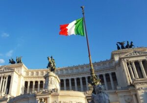 Italian flag waving in the wind in front of a government building on a bright sunny day - Italy Golden Visa