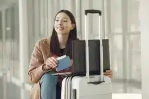 Woman sitting with her luggage, working on a laptop in an airport - Plan B passport