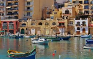 View of pier in Malta with multiple colorful boats moored in front of ancient buildings - digital nomad visa - how to pay taxes