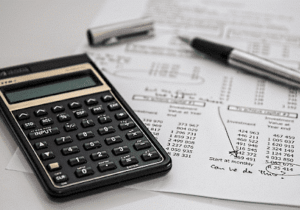 Calculator, pen, and financial documents with handwritten notes and calculations on a desk.