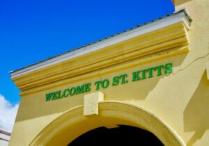 "Welcome to St. Kitts" green signage on yellow building with blue sky above - St Kitts and Nevis easiest citizenship option