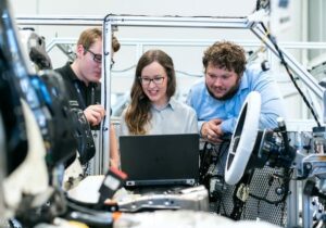 Three people working in engineering looking at a laptop.
