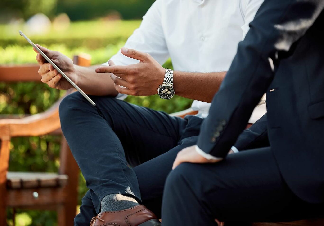 two men sitting on a bench looking at a tablet