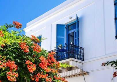 Classic white Greek building with blue shutters and colorful flowers in the foreground - best places to relocate to as an entrepreneur
