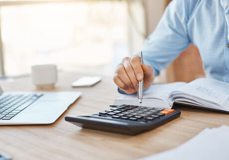 man sitting at desk using calculator and writing in a diary