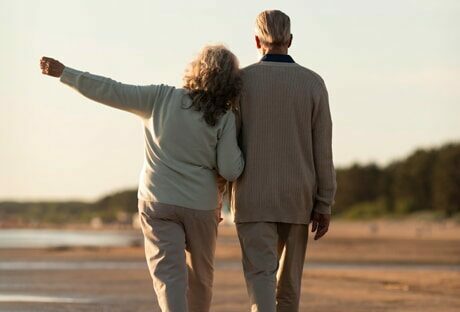 Older couple walking arm in arm along a beach on a cold day - contributing to a retirement plan to avoid paying taxes legally