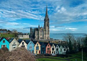 A row of colorful houses in the foreground with St. Colman's Cathedral in the background in Cobh, Ireland - small European country to retire in for American citizens