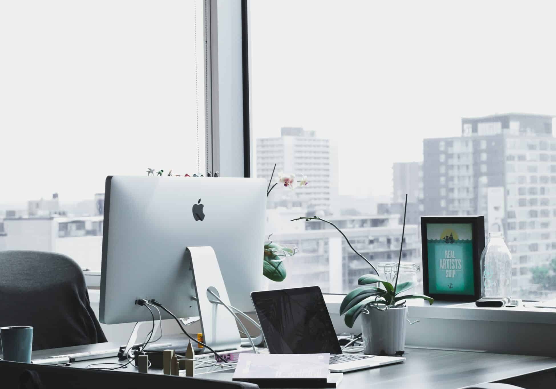 Desk with a Mac laptop and plant on it next to a window overlooking a city - offshore company formation
