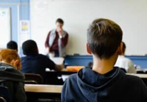 A teacher standing in front of students and a classroom. 