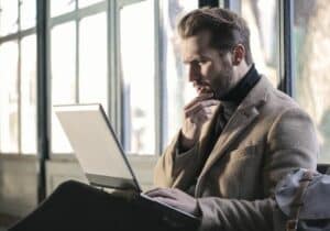 Man sitting on a couch with a laptop on his lap, pondering - online platforms for Americans to look for jobs in Europe