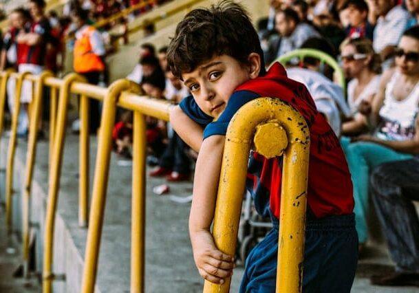 Turkish boy hanging over a yellow railing in a stadium - marriage for citizenship