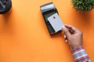 Man using a credit card on a card machine against an orange background - dual nationality taxation