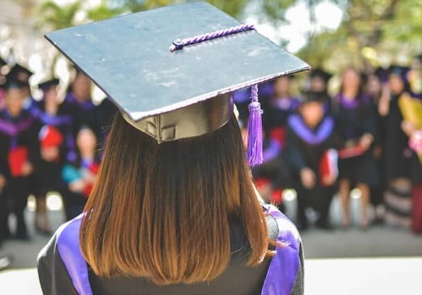 Back view of a woman wearing a graduating cap and a purple graduation sash standing in front of other graduates posing for a photo - top education systems in the world