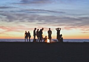 People on a beach in silhouette at sunset - Welcoming expat hubs