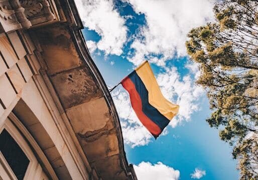 Colombian flag hanging from an old building with a partly cloudy sky in the background - marriage for citizenship