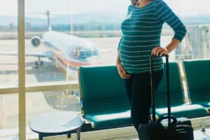 Pregnant woman standing in an airport with luggage - birth tourism