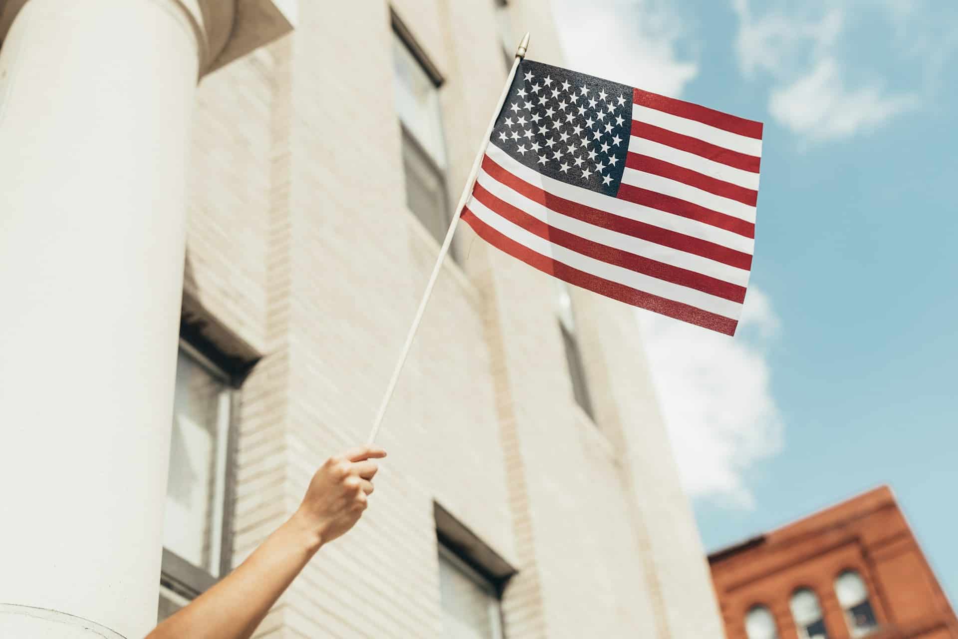 Person waving g a US flag out of a window - Plan B: Moving Abroad For Americans Webinar