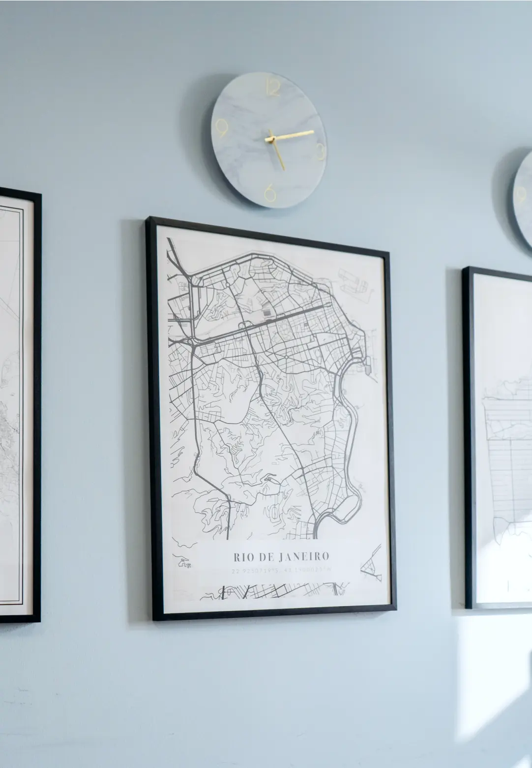Three framed maps hang on a wall beside a round clock, creating a decorative and informative display.