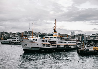 Passenger ferry docked at a busy port on the Bosphorus in Istanbul, with cityscape and cloudy sky in the background.