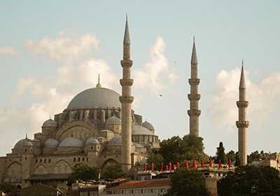 Exterior view of the Süleymaniye Mosque in Istanbul, Turkey, with its grand domes and four minarets set against a partly cloudy sky.