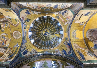 Intricate gold and mosaic ceiling of the Chora Church in Istanbul, featuring a central image of Christ surrounded by detailed biblical scenes and saints.