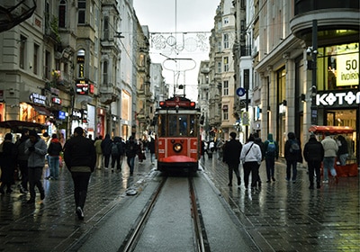 Iconic red tram on Istiklal Avenue in Istanbul, surrounded by people shopping and walking on a rainy day