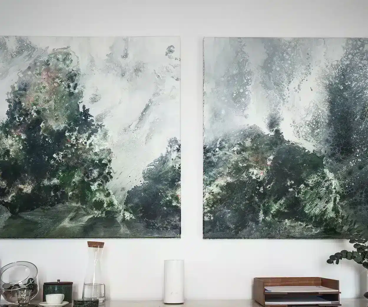 Two paintings are displayed on the wall above a table, showcasing artistic designs in a well-lit room.