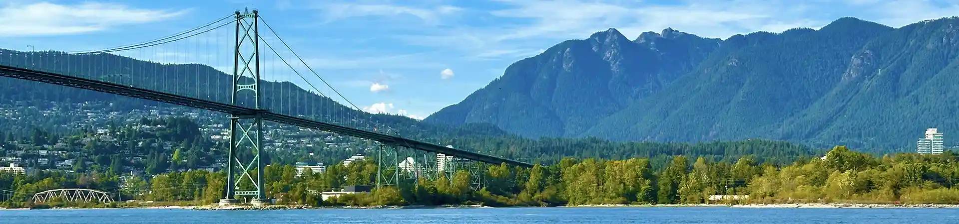 a bridge over a body of water with mountains in the background overlooking Stanley Park in Vancouver 