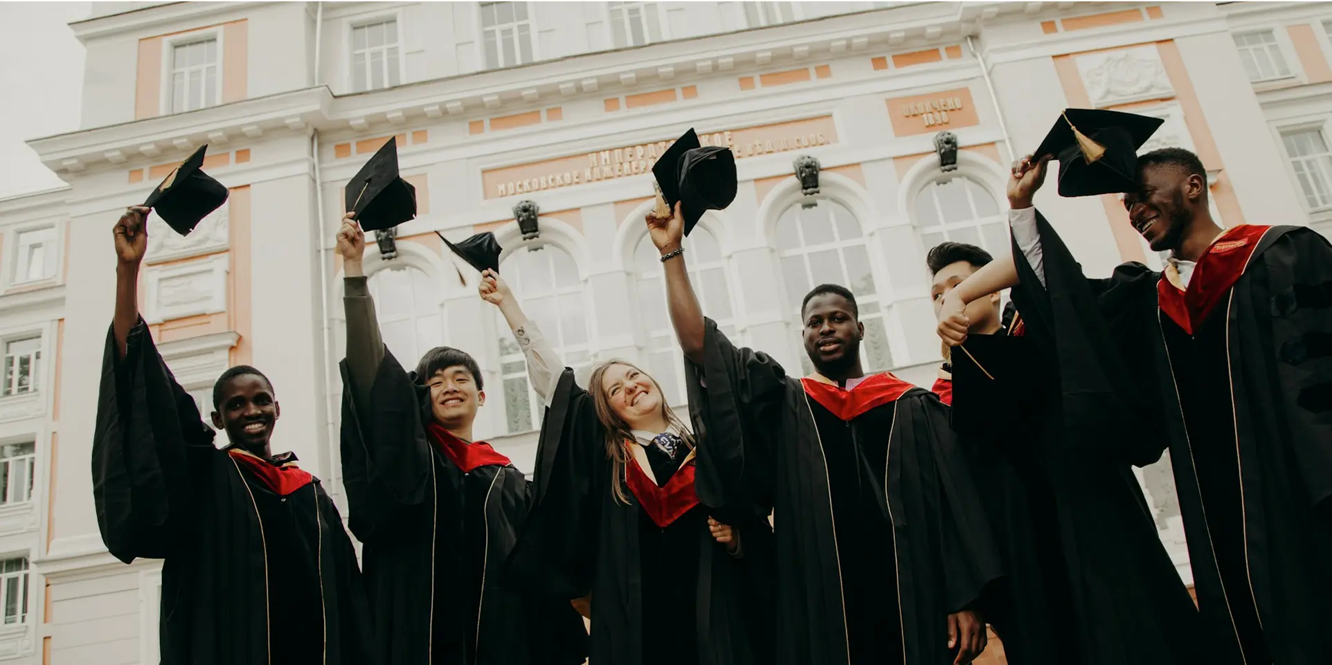 A group of graduates wearing black gowns and caps, smiling and celebrating their graduation day together.