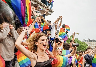 A joyful crowd waving rainbow flags and celebrating at a Pride event outdoors.