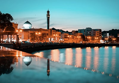 Town of Mutrah, Muscat in Oman at dusk with buildings and lights reflecting on water - Middle Eastern countries that are safest