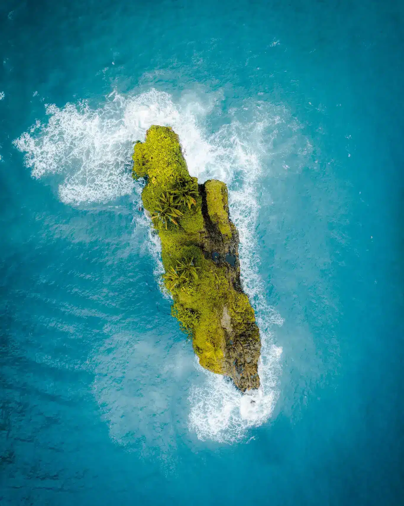 Aerial view of a small island surrounded by blue ocean waters, showcasing lush greenery and sandy beaches.
