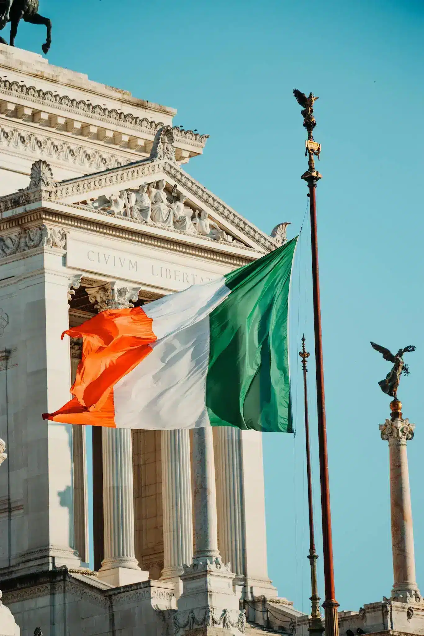 A large Irish flag waves proudly in front of a building, showcasing its vibrant green, white, and orange colors.