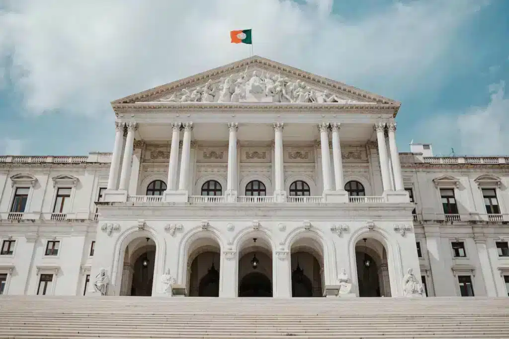 Fachada de um grande prédio branco com uma bandeira hasteada bem à frente.
