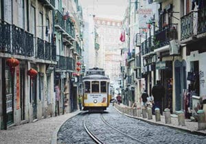 Historic yellow tram moving through a narrow, cobblestone street lined with old buildings and balconies in Lisbon, Portugal - least racist countries in the world