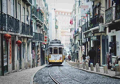 Historic yellow tram moving through a narrow, cobblestone street lined with old buildings and balconies in Lisbon.