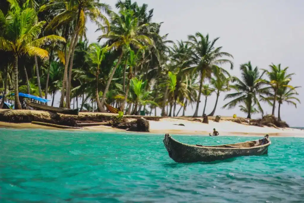 Um barco está ancorado na praia arenosa de uma ilha tropical na Guiné, cercado por uma vegetação exuberante e águas azuis cristalinas.