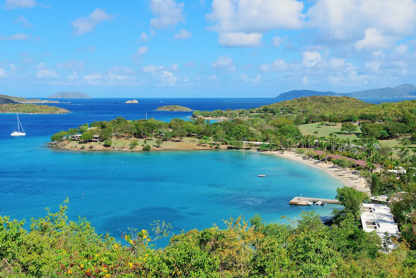 A scenic view of the beach and ocean from a hill, showcasing the coastline and waves under a clear blue sky.
