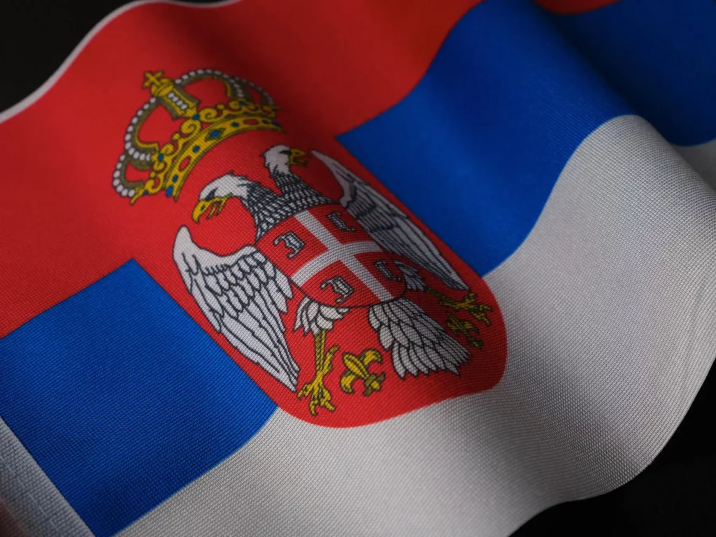 Serbia's flag displayed up close, featuring red, blue, and white horizontal stripes with a coat of arms on the left.