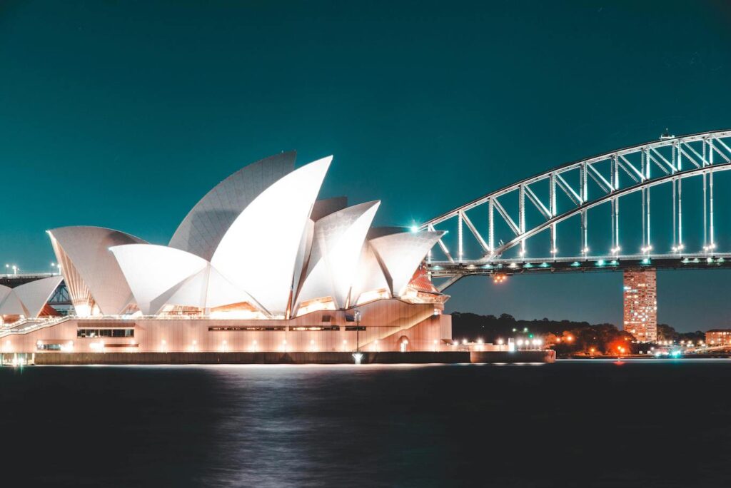 Sydney Opera House and Harbour Bridge illuminated at night, showcasing their iconic architecture against a dark sky.