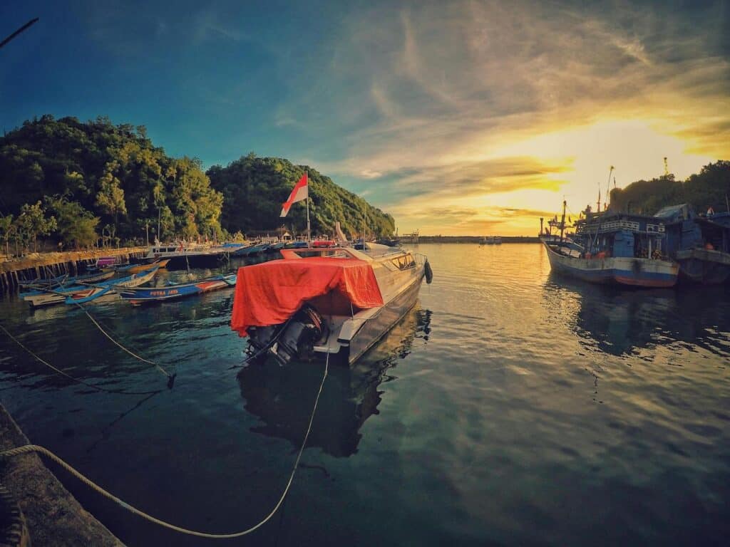 A boat docked at the water, covered with a red cloth, surrounded by calm water and a clear sky.